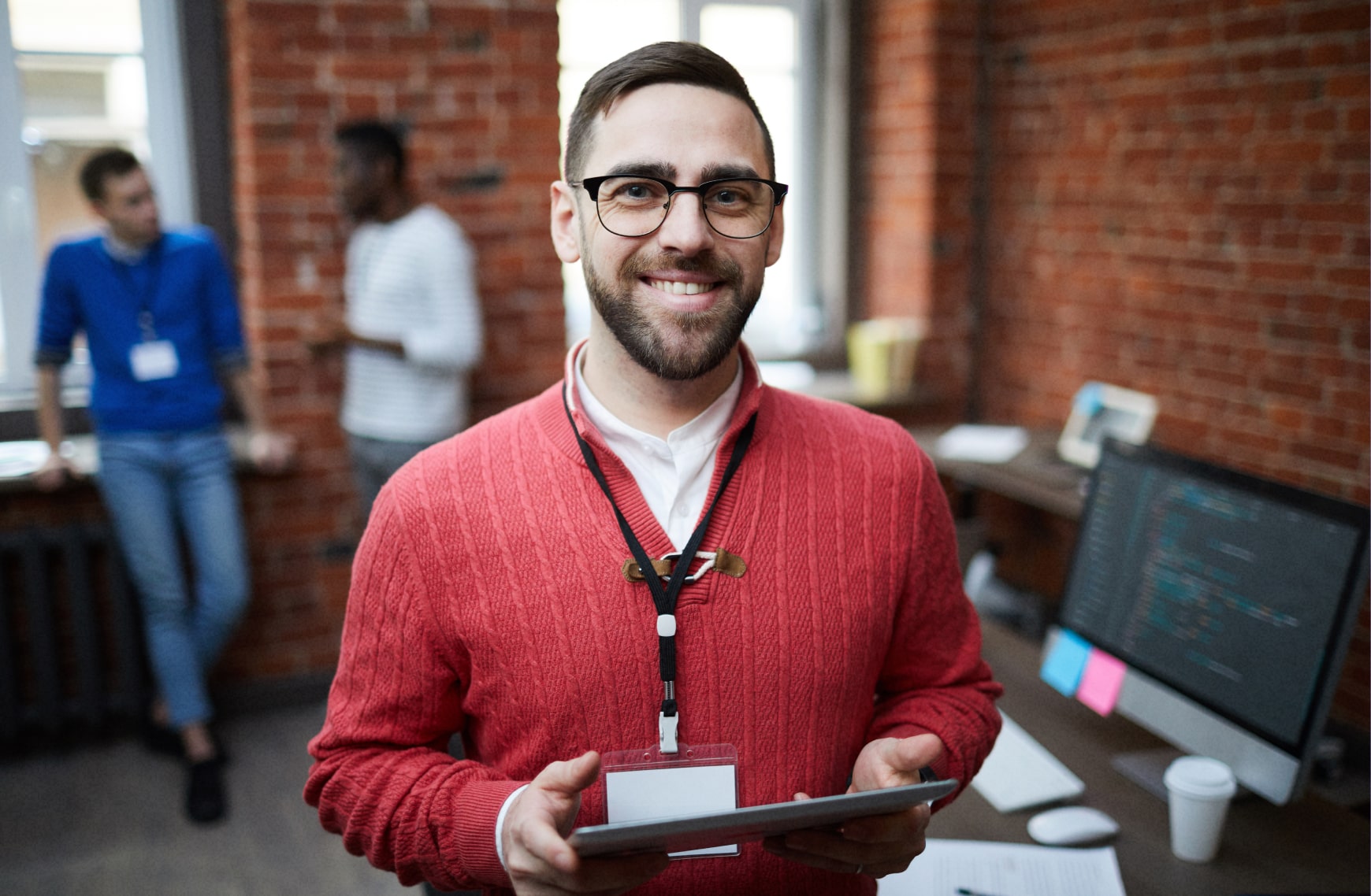 Young caucasian project manager, holding tablet in office with coworkers behind him