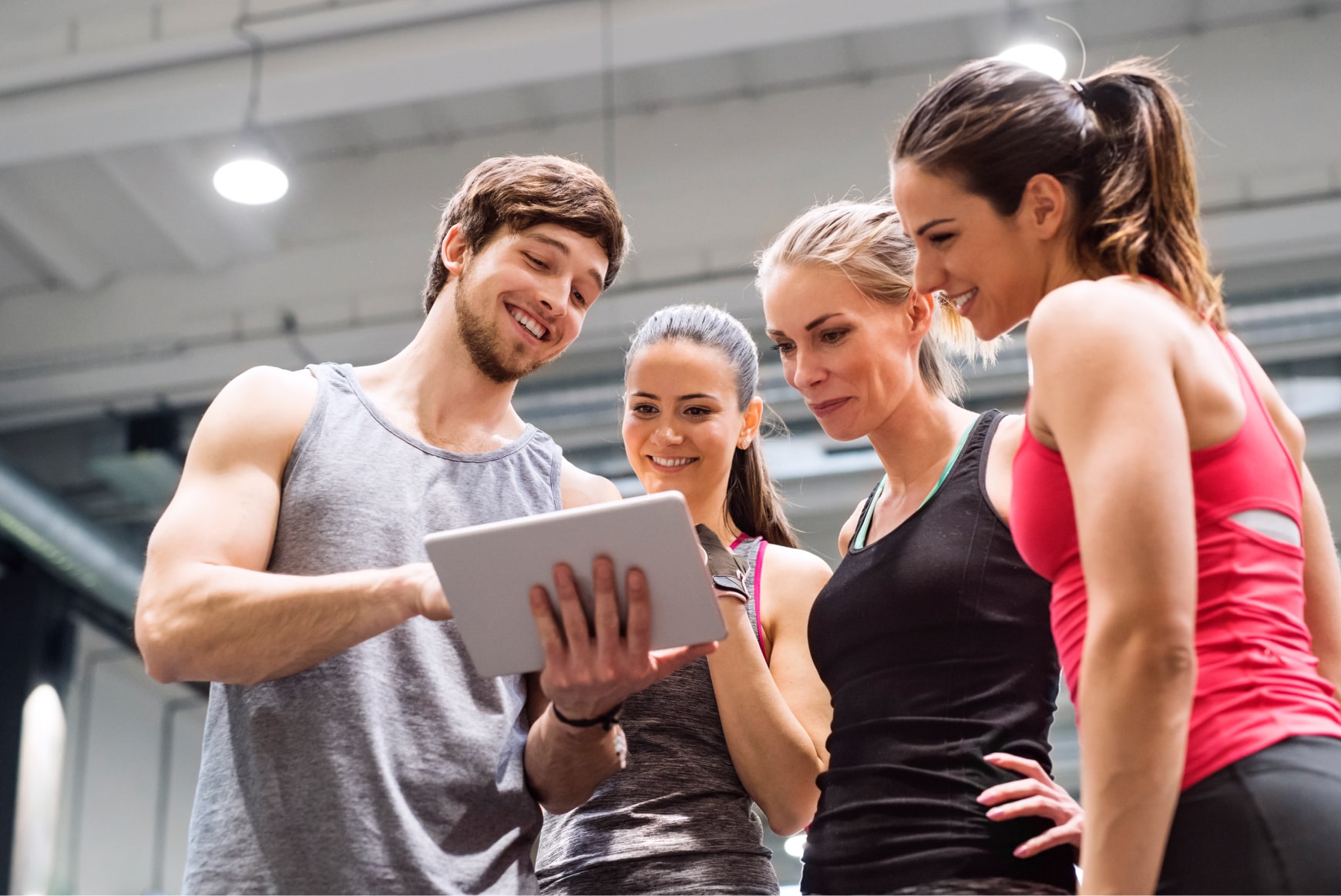 A trainer getting feedback on a tablet from a group of happy gym-goers.