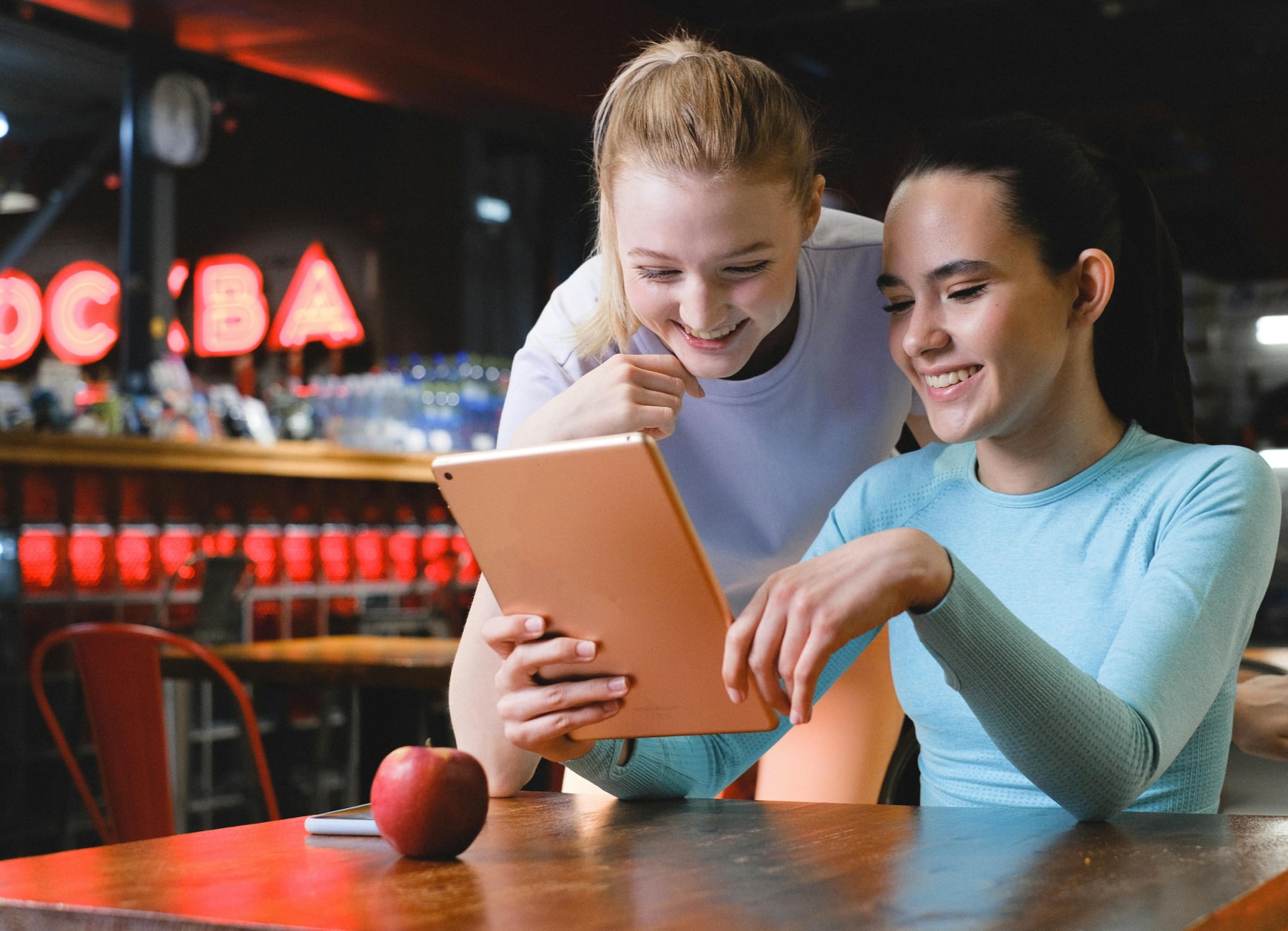Fitness studio staff member showing a customer a schedule on a tablet with visible class options, highlighting personalization and connection in a modern gym setting.